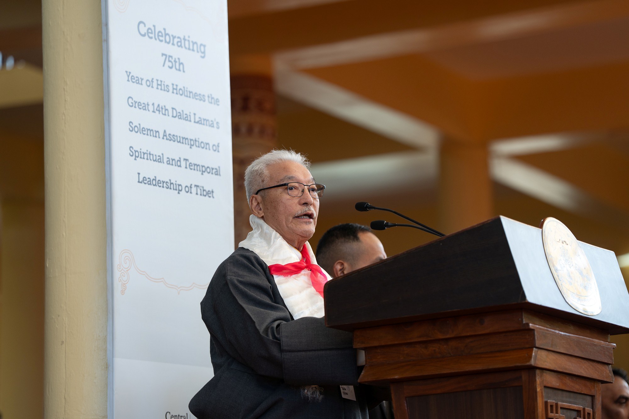 Төвөдийн гол хийдийн талбайд Дээрхийн гэгээн Далай лам Төвөдийн шашин ба төрийн удирдлагыг хүлээн авсны 75 жилийн ойг тэмдэглэх ёслолын үеэр төвөд сургууль төгсөгчдийн зохион байгуулах хорооны дарга Таши Намгял үг хэлж байгаа нь. 2025.11.17. Энэтхэг, Х.П., Дарамсала. Зургийг: Тензин Чойжор.